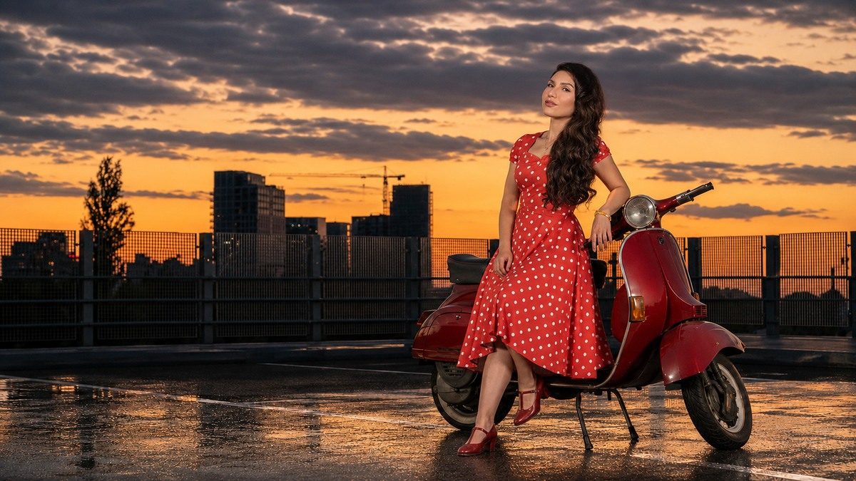 Anna in een rode jurk met witte stippen bij een rode klassieke Vespa tijdens zonsondergang in Eindhoven